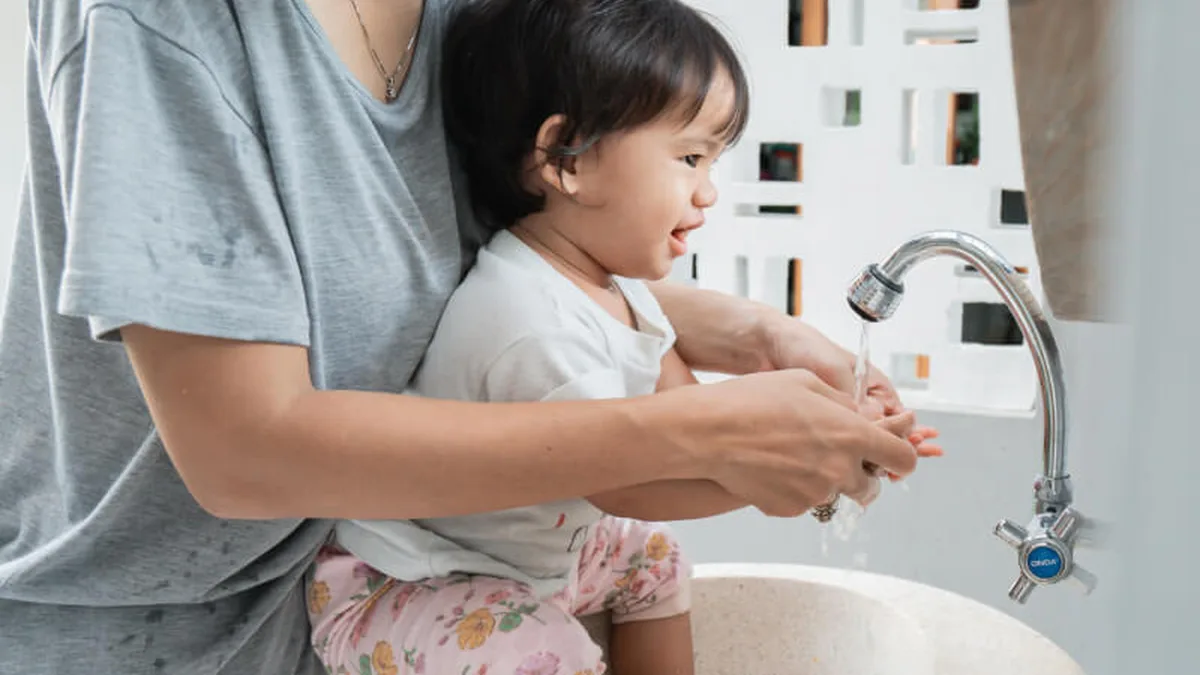 Une mère aide son jeune enfant à se laver les mains au-dessus d&rsquo;un lavabo