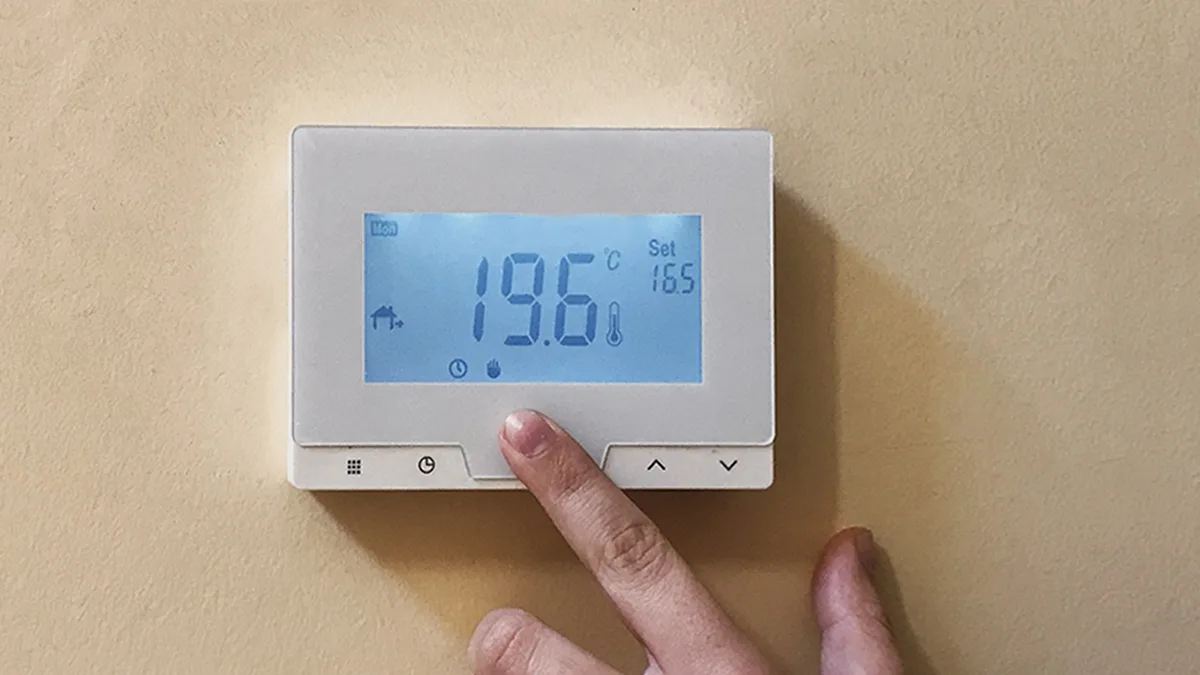 Une main règle un thermostat d&rsquo;ambiance affichant 19,6 °C