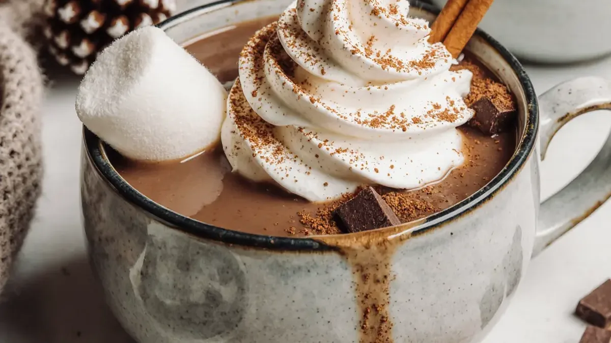 Un chocolat chaud fumant avec de la chantilly, un bâton de cannelle et un chamallow