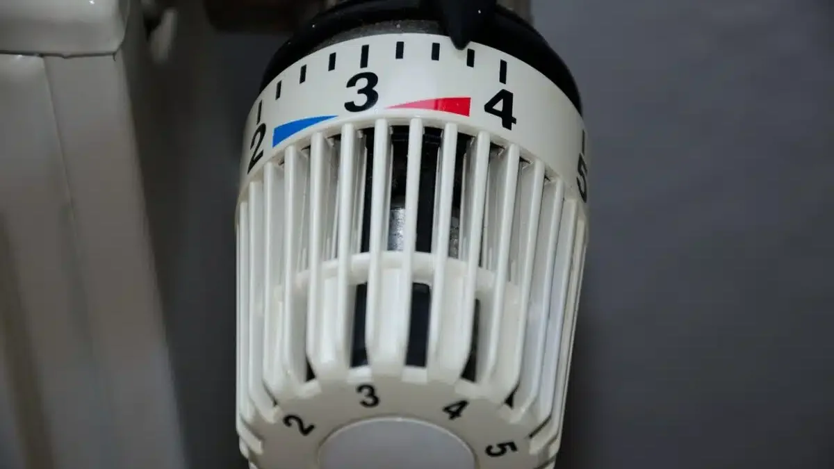 Une main règle la vanne thermostatique d&rsquo;un radiateur