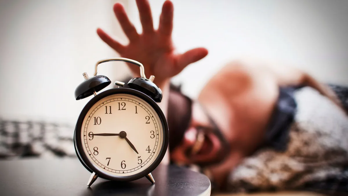 Une main hésite à éteindre le réveil, symbole des matins difficiles