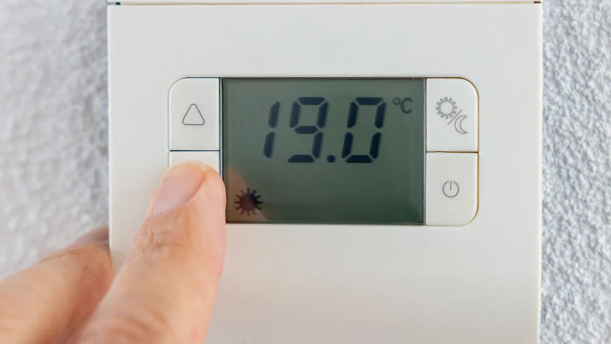 Une main règle un thermostat affichant 19 degrés