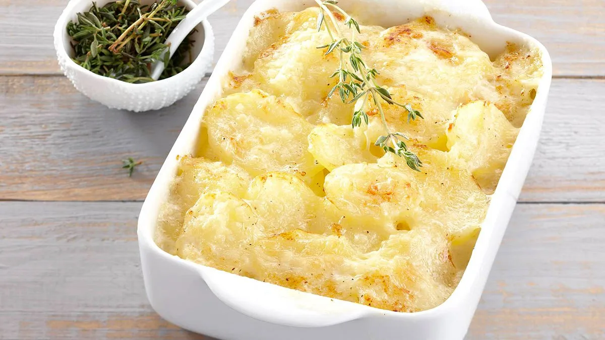 Plat rectangulaire de gratin dauphinois parsemé de thym, prêt à être servi