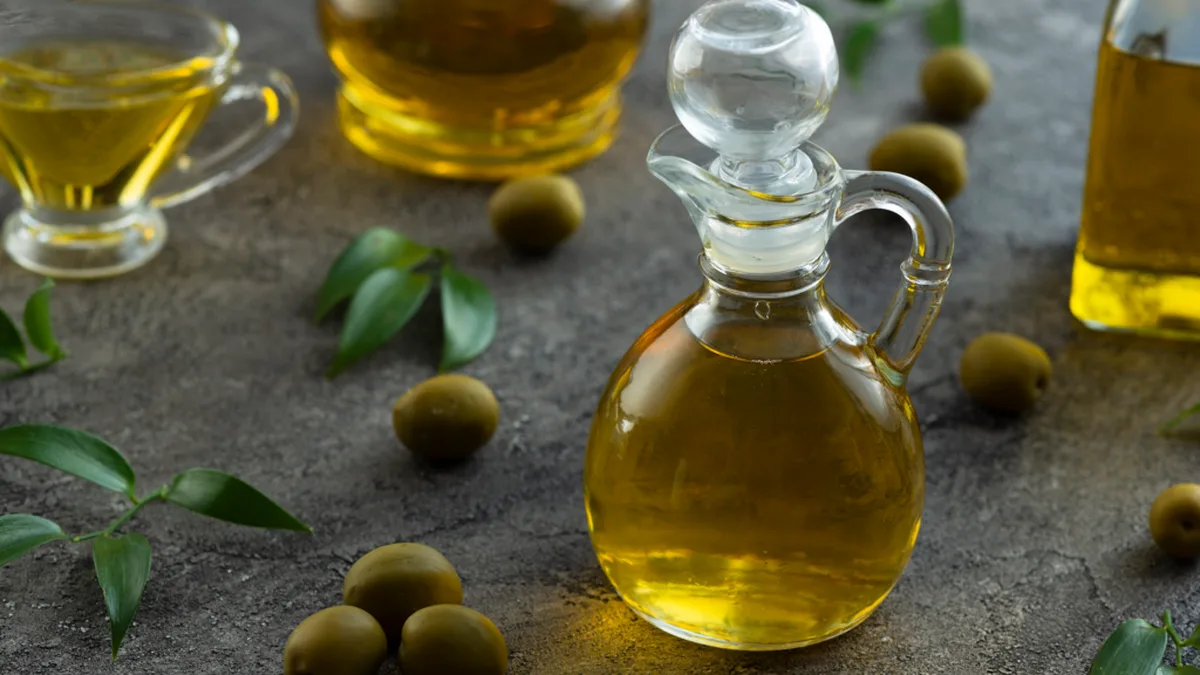 Plusieurs bouteilles et burettes d&rsquo;huile d&rsquo;olive dorée, entourées d&rsquo;olives vertes
