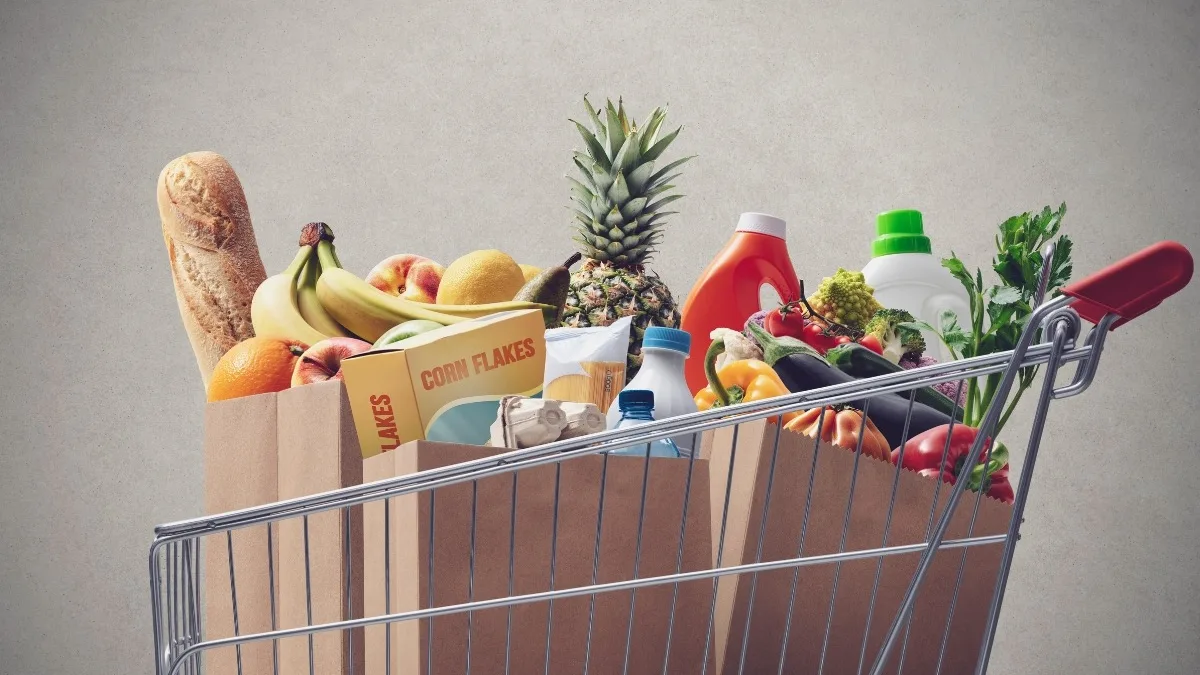 Un caddie rempli de courses, avec une baguette, des fruits et des légumes