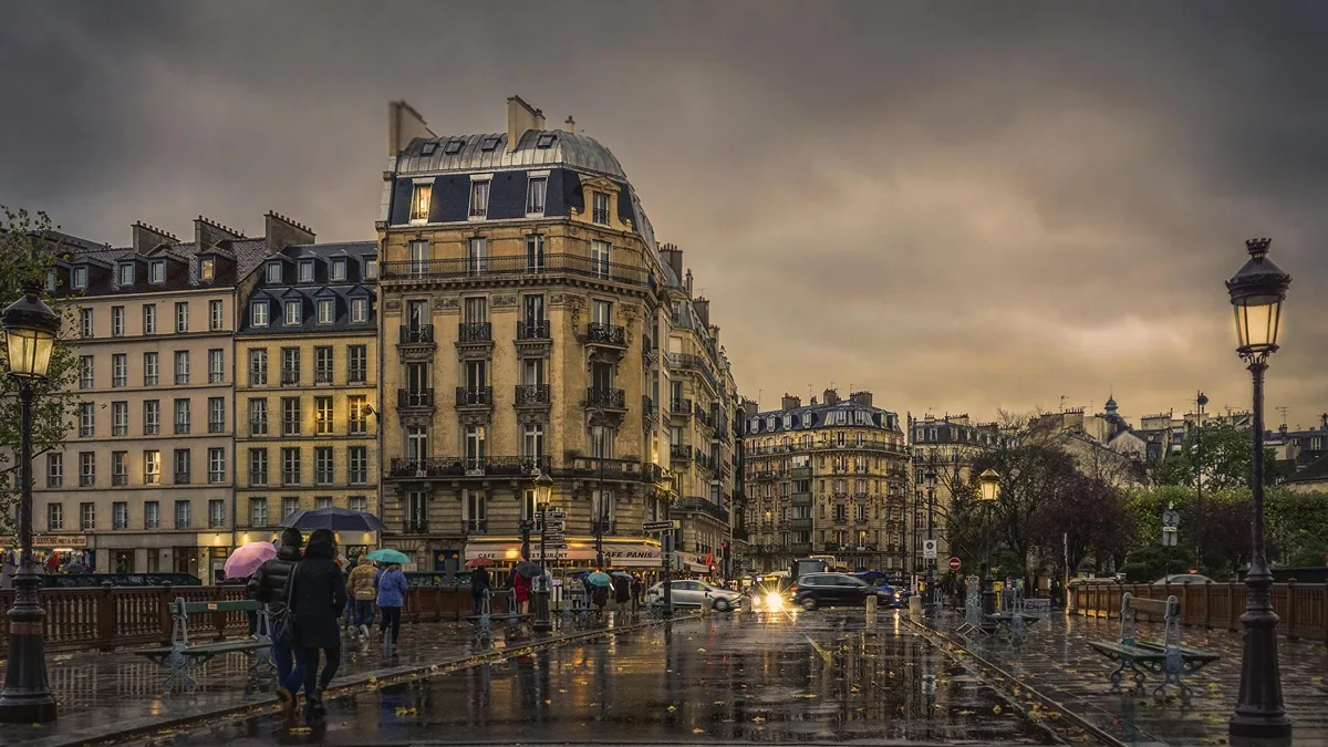 Des piétons sous la pluie dans une rue parisienne, parapluies ouverts sur un trottoir détrempé