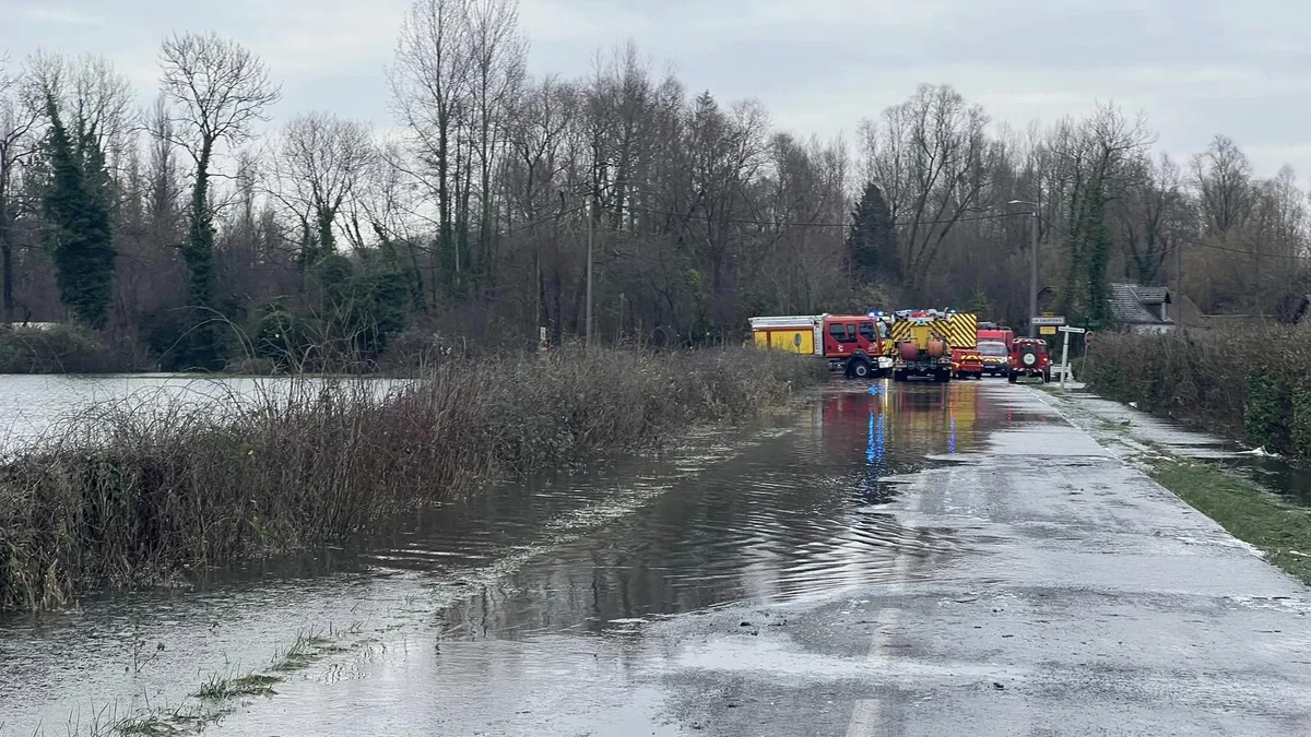Une route inondée, avec des véhicules de secours au loin, dans le Pas-de-Calais