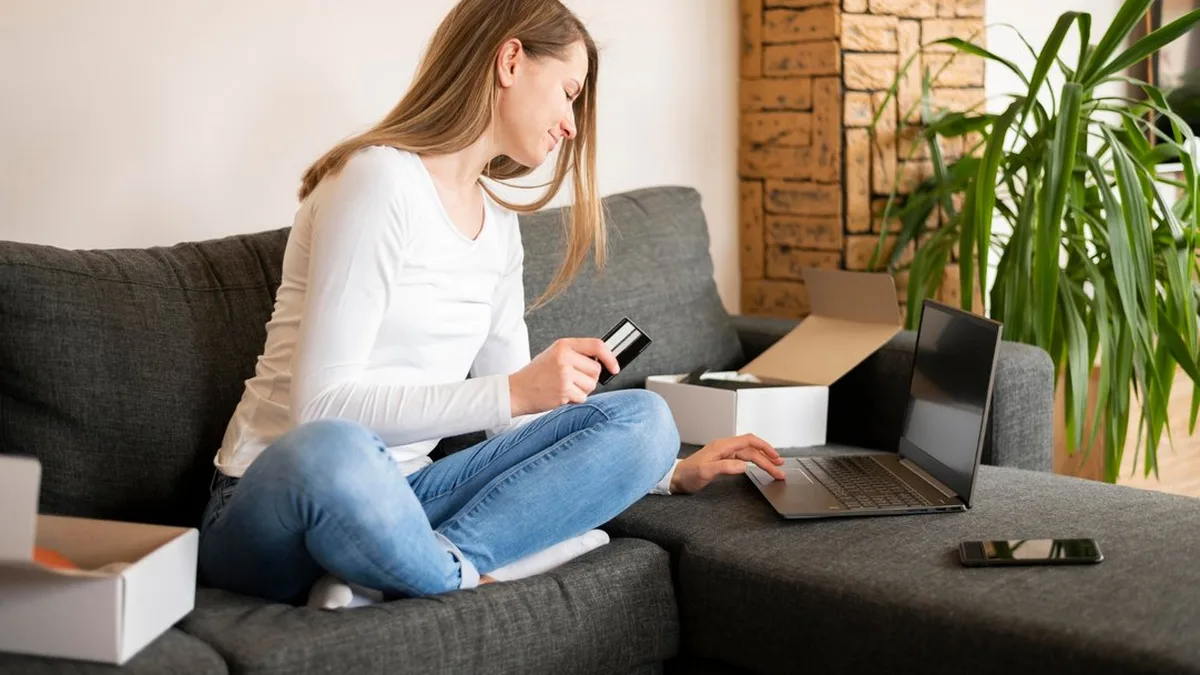 Une femme paie un achat en ligne avec sa carte bancaire depuis son canapé