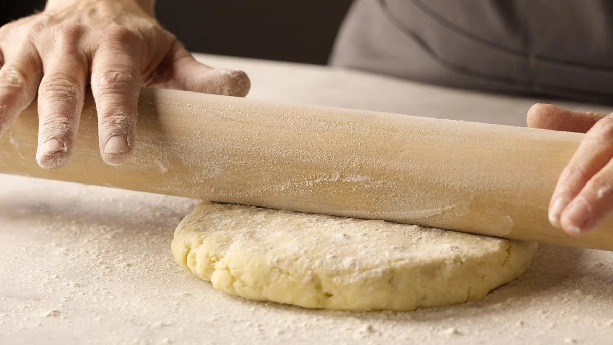 Mains étalant une pâte à tarte au rouleau sur un plan fariné