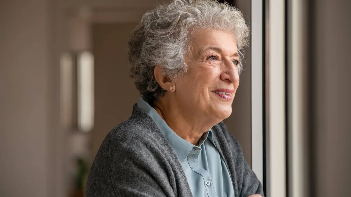 Une femme âgée regarde par la fenêtre de son logement