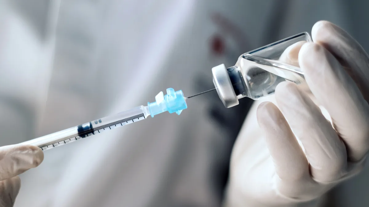 Une seringue prélève une dose dans un flacon de vaccin : le format multidose impose du matériel d&rsquo;injection
