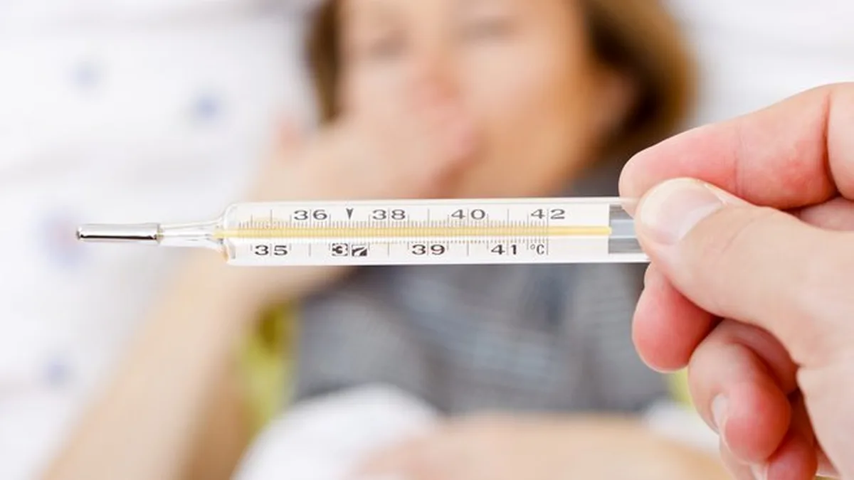 Un thermomètre tenu devant un enfant malade alité, la fièvre étant le signe le plus surveillé de la grippe