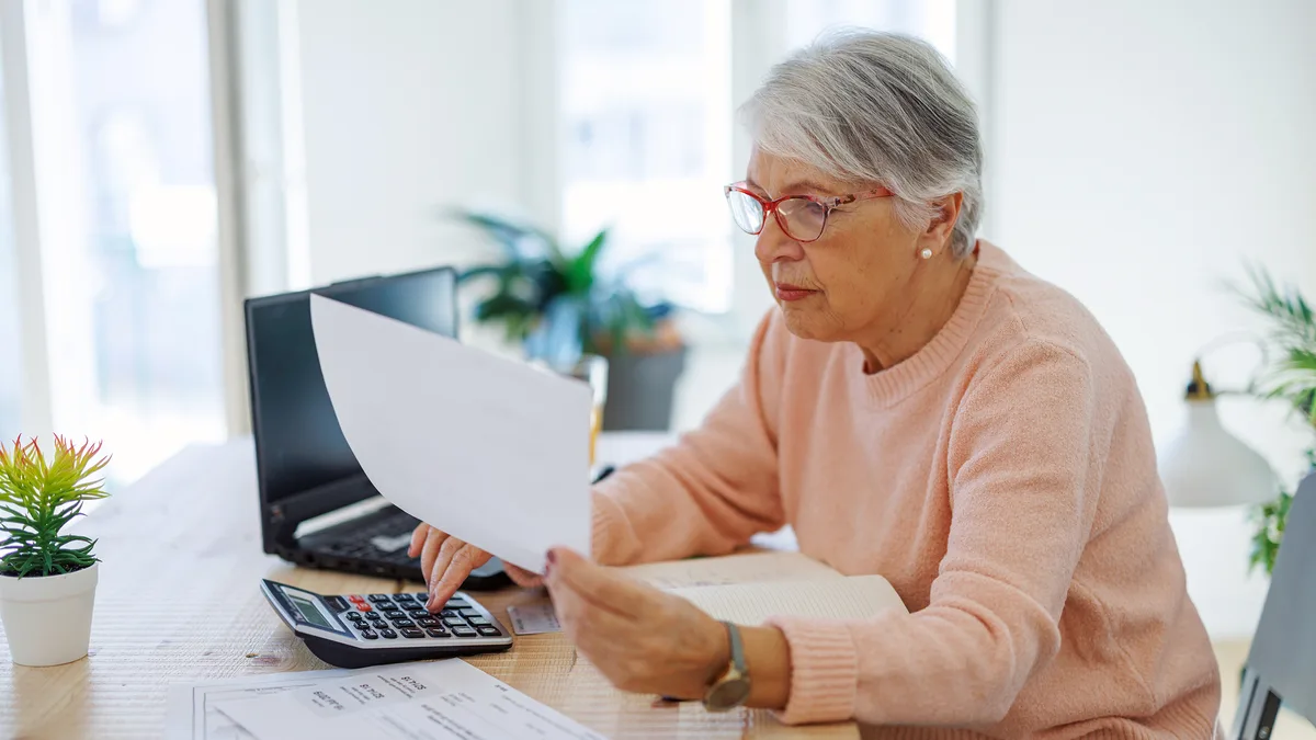 Une retraitée vérifie ses documents fiscaux avec une calculatrice