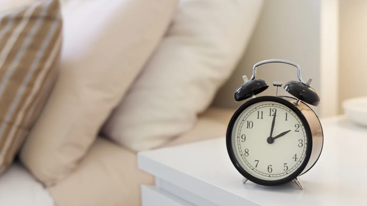 Un réveil sur une table de nuit, à côté d&rsquo;un lit