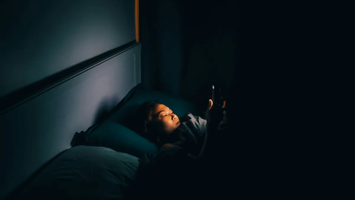 Une personne consulte son téléphone au lit, dans le noir